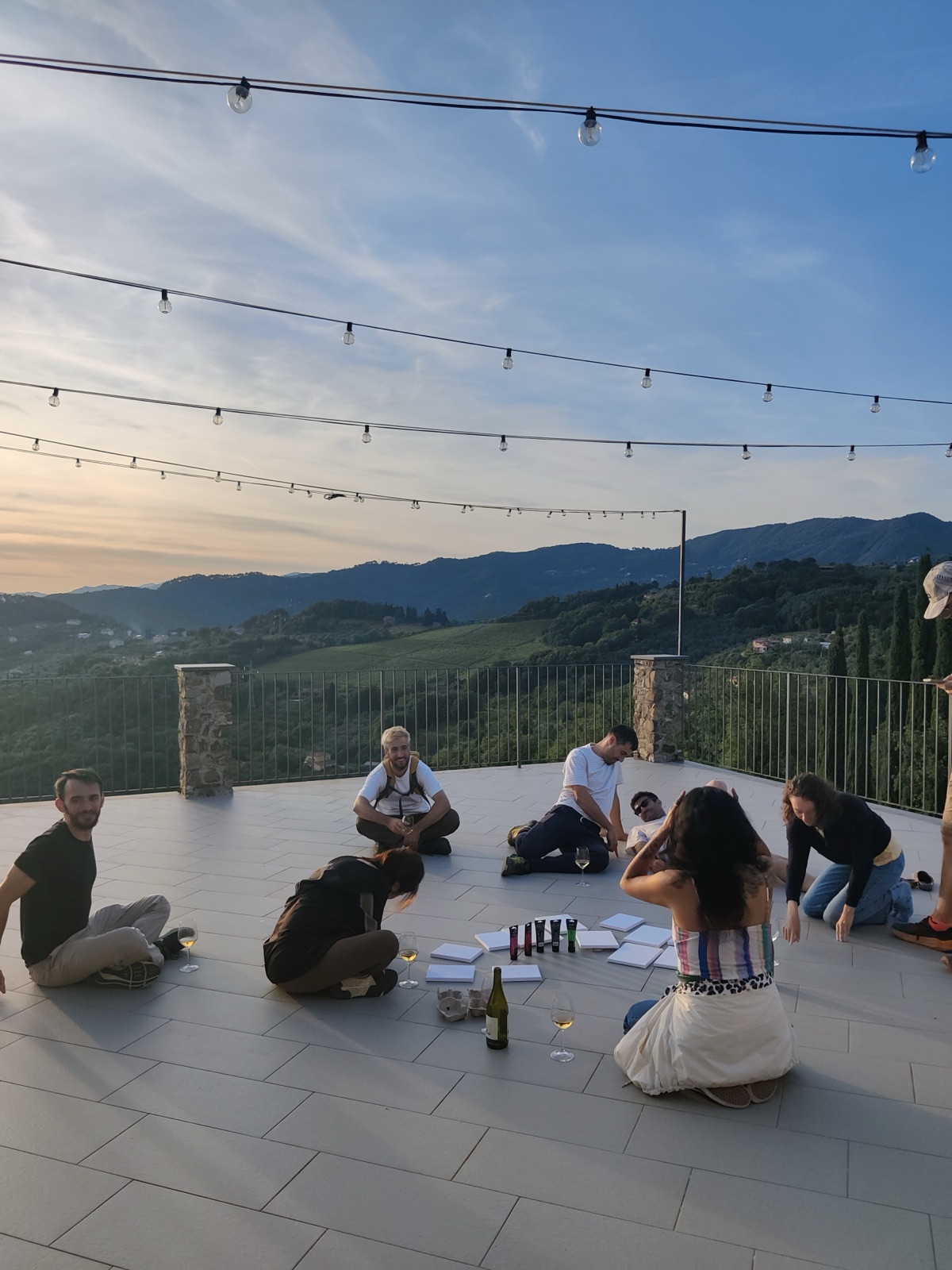 People painting together on a terrace overlooking vineyard hills at dusk during the Slowlit pilot